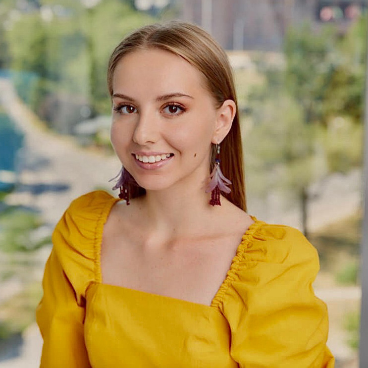 Kateryna has straight blonde hair, a big smile and is wearing a yellow dress.